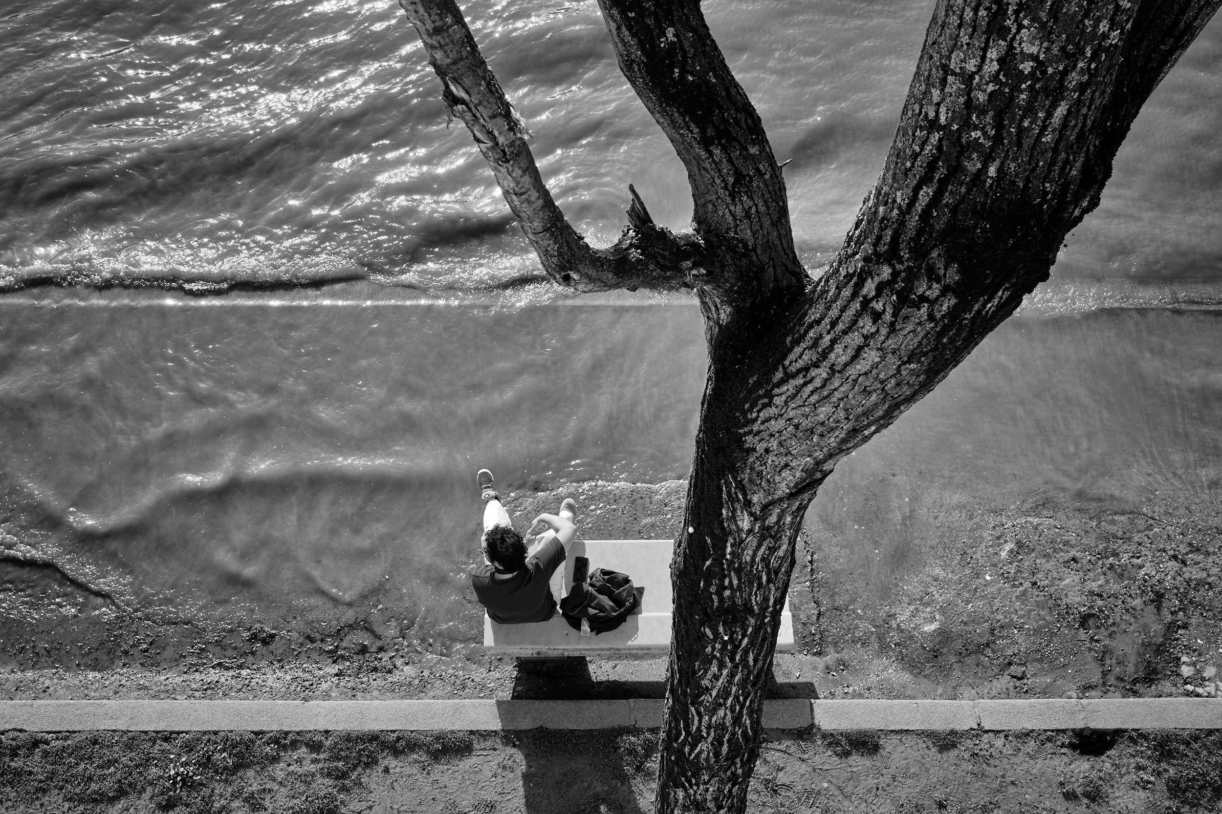 Paris - A person sat quietly on a bench by the river Seine, watching the water slowly rise with the tide.